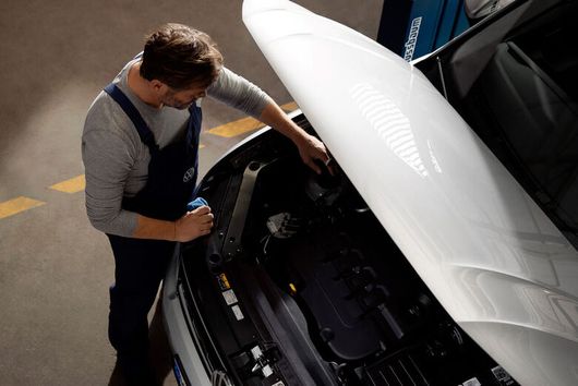 VW-Mitarbeiter prüft weißes Auto mit geöffneter Motorhaube