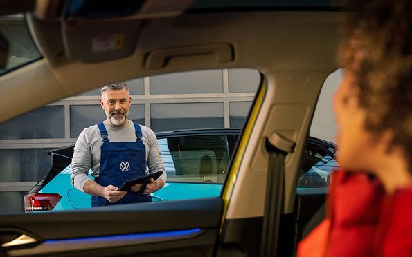 Frau redet mit VW-Mitarbeiter der vor Auto steht